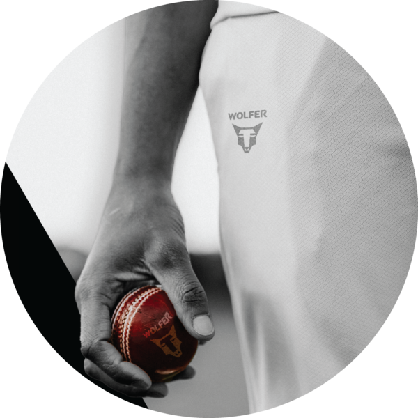 Close‑up of cricketer's hand holding a Wolfer red leather cricket ball ready to bowl
