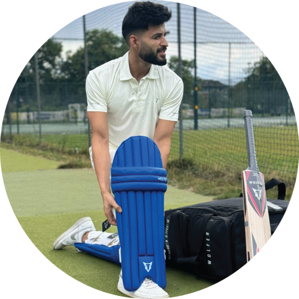 Cricketer wearing Wolfer blue ambidextrous leg guards kneeling on turf with kit bag and bat
